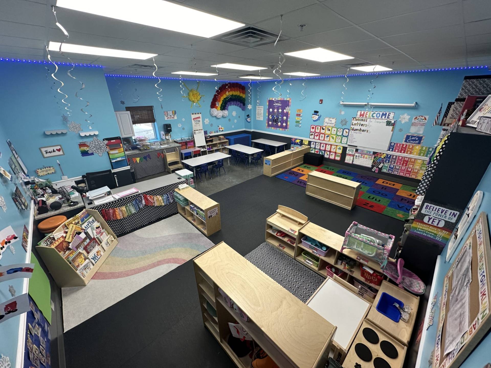 A colorful infant and toddler classroom with a rainbow mural and learning materials